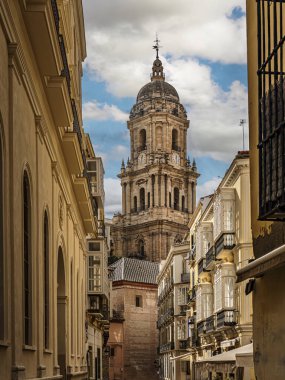Çerçevelenmiş cepheler ve balkonlar tarafından çerçevelenmiş güneşli bir cadde, tarihi bir mimari olan Malaga, İspanya 'yı harmanlayan büyük Malaga Katedrali' ne doğru gözlere rehberlik eder.