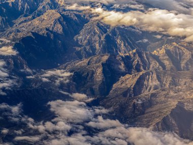 Tırtıklı uçurumlar arasında yumuşak bulutların dolaştığı yüksek tepelerin ve derin vadilerin kuş bakışı görüntüsü.