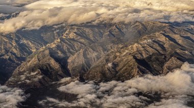 Bulutların üzerinde yükselen engebeli tepeleri olan geniş bir dağlık arazi. Ilık gün doğumu dokuyu ön plana çıkarır ve macera, yalnızlık ve doğanın muazzam boyutunu yaratır..