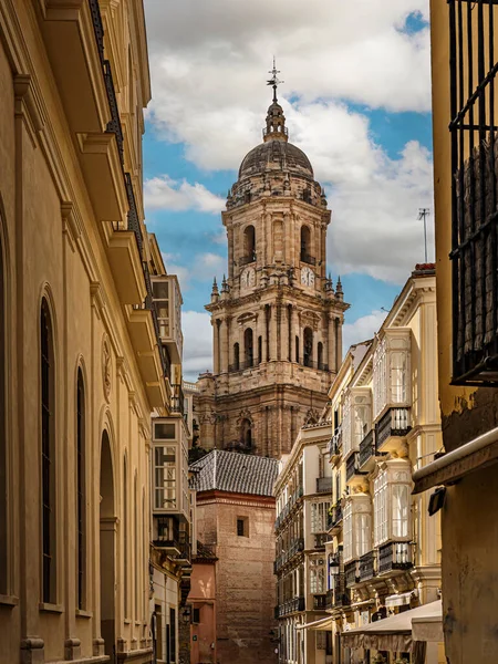 Çerçevelenmiş cepheler ve balkonlar tarafından çerçevelenmiş güneşli bir cadde, tarihi bir mimari olan Malaga, İspanya 'yı harmanlayan büyük Malaga Katedrali' ne doğru gözlere rehberlik eder.