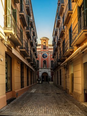 Sıcak tonlu apartman balkonlarının çerçevelediği sessiz, güneşli dar bir cadde süslü camları ve kaldırımları olan tarihi bir kilise cephesine götürür, Malaga İspanya