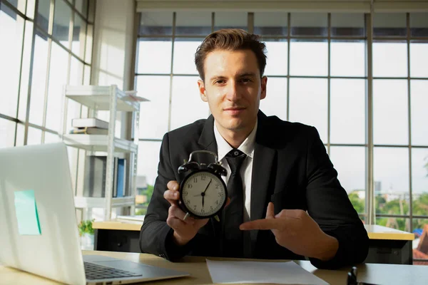 Businessman holding alarm clock for show overtime his job.Work late office.Employee working late in company.