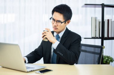 Ciddi Asyalı işadamı ofiste çalışıyor ve kahve içiyor.