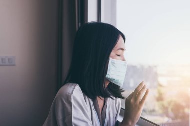 Depresyondaki Asyalı kadın hasta ayakta duruyor ve hastane penceresinden bir şeye bakıyor.