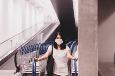 Alışveriş merkezindeki virüs salgını sırasında cerrahi maske takıp alışveriş yapan güzel Asyalı kadın.