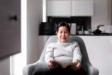 Evde kitap okuyan yaşlı Asyalı kadın, dinlenme zamanı, yaşlılar yaşam tarzı konsepti, uzun görüş.