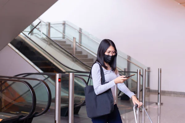 Asian woman wearing face mask and using mobile phone during coronavirus pandemic in the mall