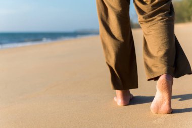 Gün batımında, arka plan, tatil ve tatil konsepti boyunca sahilde yürüyen çıplak ayaklı kadına yakın durun.