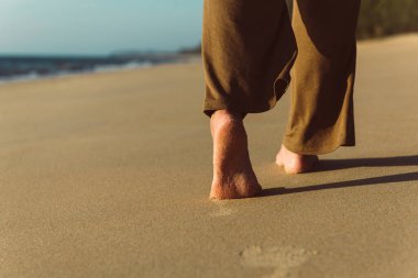 Gün batımında, arka plan, tatil ve tatil konsepti boyunca sahilde yürüyen çıplak ayaklı kadına yakın durun.