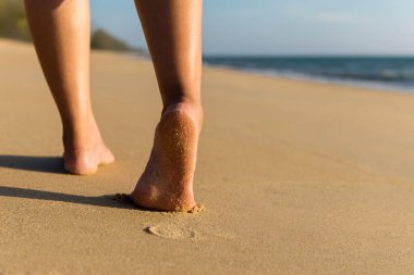 Gün batımında, arka plan, tatil ve tatil konsepti boyunca sahilde yürüyen çıplak ayaklı kadına yakın durun.