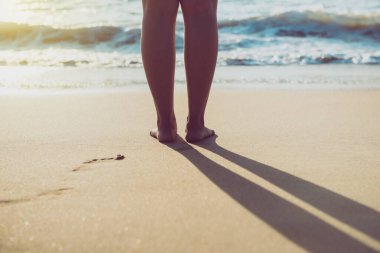 Gün batımında, plajda duran çıplak ayaklı kadına yakın durun. Tatil ve tatil kavramı.