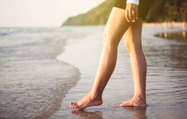 Gün batımında, sahilde yürüyen çıplak ayaklı kadınları, tatilleri ve tatil kavramlarını kapatın.