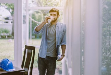 Mimar adam modern ofiste kahve içiyor, mutlu ve gülümsüyor.