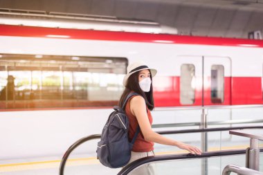 Yüz maskesi takan Asyalı kadın tren istasyonunda yürüyen merdiven kullanıyor toplu taşımada güvenlik, covid-19 salgını sırasında yeni bir normal.