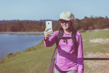 Sırt çantalı, cep telefonlu bir kadın selfie 'si, mutlu ve gülümseyen, kamp yapma konsepti.