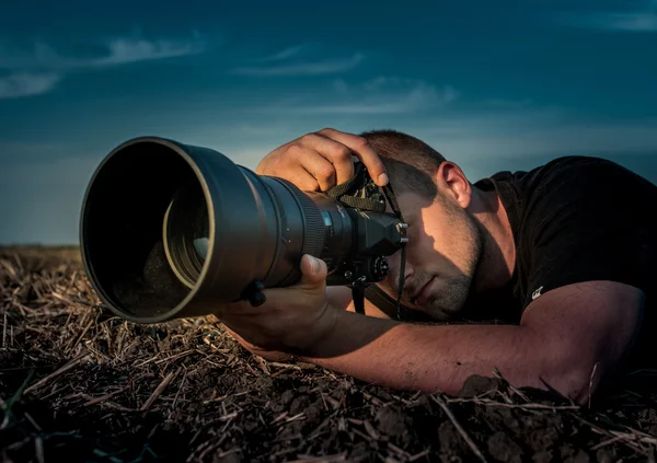Jovem fotógrafo segurando câmera em campos de milho no pôr do sol quente — Fotografia de Stock