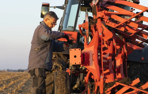 Mechanic fixing plow on the tractor. Improvement, work.