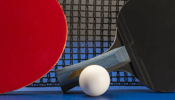 两个乒乓球球拍和一个蓝色桌子上的球网 — 图库照片