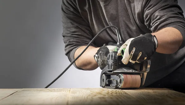 Carpenter works with belt sander in carpentry