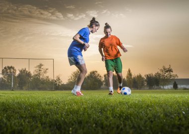 Gün batımında sahada iki bayan futbolcu.