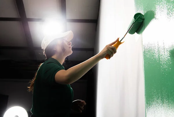 Young women painter in shirt  painting a wall with paint roller