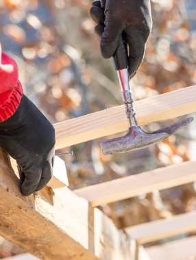 İnşaat işçisi marangoz çatıya çekiçle tahta çakıyor.