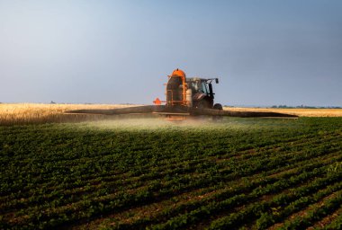 Traktör gün batımında yemyeşil bir alanda soya püskürtüyor..