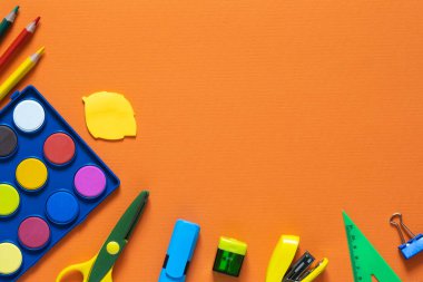 Okul konseptine geri dönelim. Okul ve ofis malzemeleri masanın üzerinde. Turuncu arkaplan. Fotokopi alanı ile düzleştirilmiş.