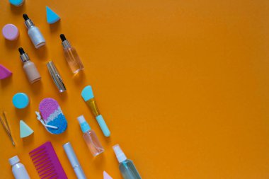 Turuncu arka planda kozmetik ürünleri olan düz kompozisyon. Çok renkli süngerler. Kadınların kendi kendilerine bakmaları. Kopyalama alanı olan en üst görüntü.