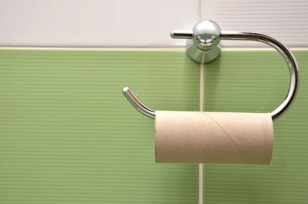 Пустой рулон на держателе туалетной бумаги с белой и зеленой плиткой на заднем плане — стоковое фото