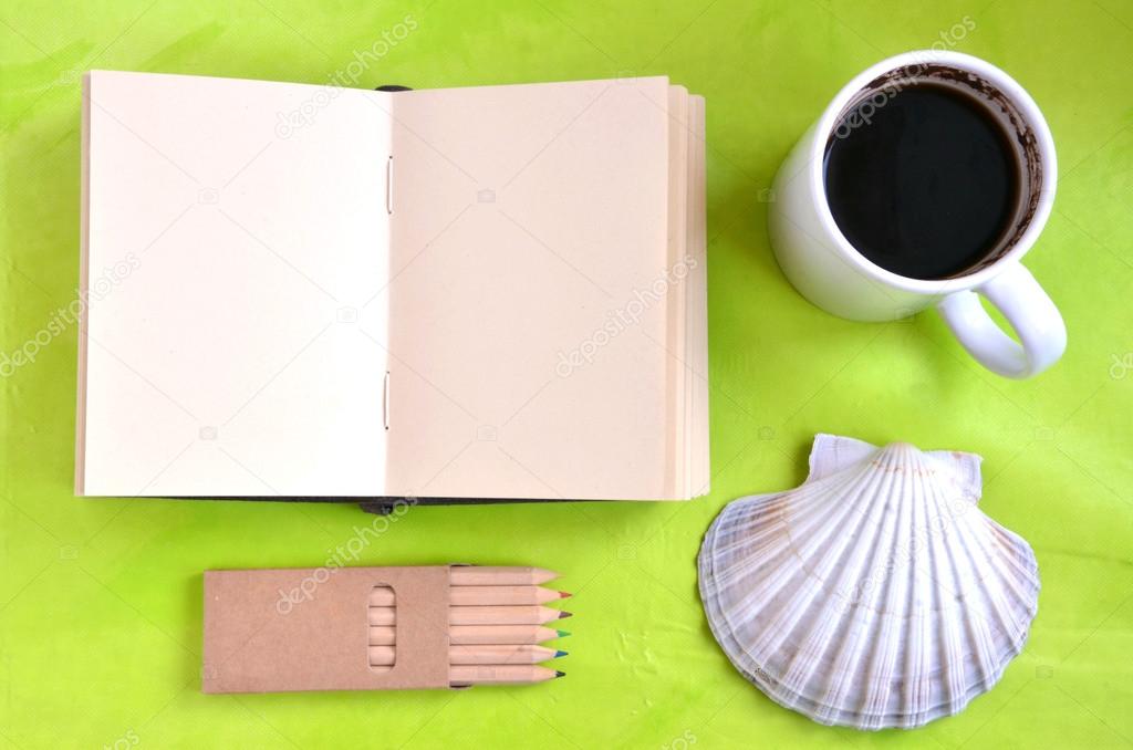 Notebook, shell, cup of coffee and pastels on green background (flat lay)