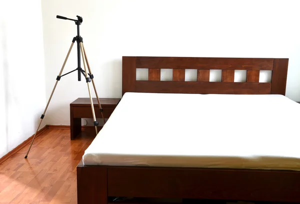 Tripod for camera next to the wooden bed in bedroom — Stock Photo, Image