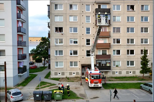 Bombeiros em ação, dois homens uprise em cesta de lança telescópica de caminhão de bombeiros. Algumas pessoas estão assistindo, bloco de apartamentos no fundo . — Fotografia de Stock