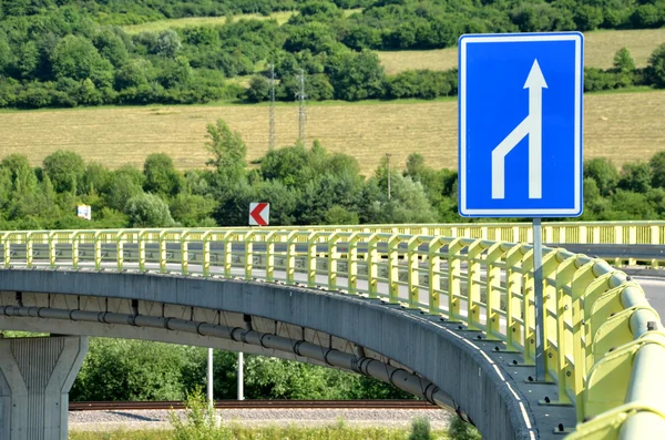 Вигнута годівниця дорога в сільській місцевості, біла стрілка дорожнього знака на передньому плані — стокове фото