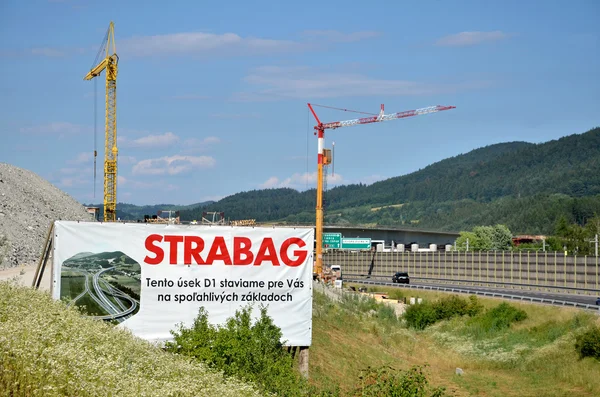 Zwei Turmdrehkräne auf der Baustelle der slowakischen Autobahn d1, im Vordergrund die Werbetafel der Baufirma Strabag — Stockfoto