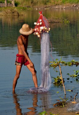 Mandalay. Myanmar. 21 Kasım 2016. Hasır şapkalı genç bir balıkçı Taungtaman Gölü 'ne ağ örüyor. Bu, gölün yerlilerinin geleneksel balık tutma yöntemidir..
