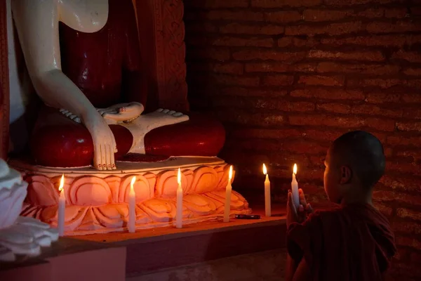 バガン ミャンマー 2016年11月26日 手にろうそくを持った色の笠を被った少年僧が 仏教寺院の仏像の前でお祈りを読みます — ストック写真