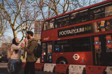 Shepherd 's Bush, Londra -124; İngiltere - 2021.03.22: Kırmızı çift katlı otobüsün önünde eğlenen sevimli mutlu çift