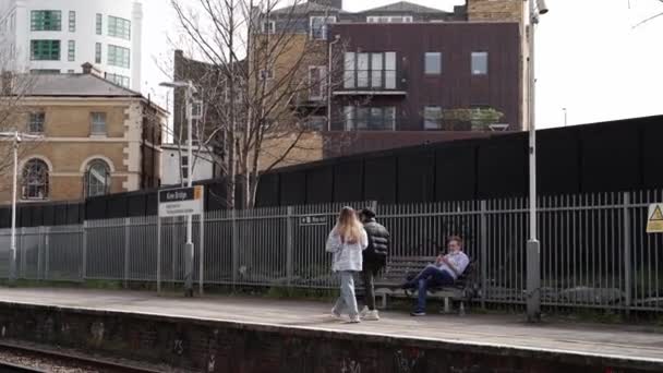 Muž sedící na lavičce u prázdné stanice Kew Bridge a čekající na vlak během uzamykání Coronaviru. Lidé projíždějící. — Stock video