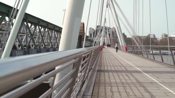 Persone a piedi il ponte di Hungerford e Golden Jubilee Bridges nella giornata di sole durante il blocco pandemico di Coronavirus — Video Stock