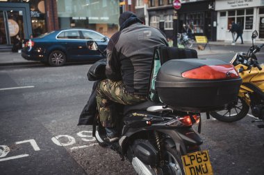 Soho, Londra the 124; İngiltere - 2021.04.16: Yeni düzen için scooter 'da oturan teslimatçı sürücü. Kargo Servisi