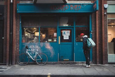 Soho, Londra the 124; İngiltere - 2021.04.16: Yeni düzeni bekleyen bisikletli teslimatçı adam şoförü. Kargo Servisi