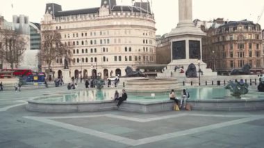 İnsanlar Coronavirus Kilitlemesi sırasındaki güneşli bahar gününde Trafalgar Meydanı çeşmelerinde takılıyor.