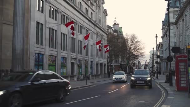 Bendera Kanada melambaikan tangan dari Komisi Tinggi Kanada di Britania Raya sementara mobil-mobil yang lewat di jalan — Stok Video