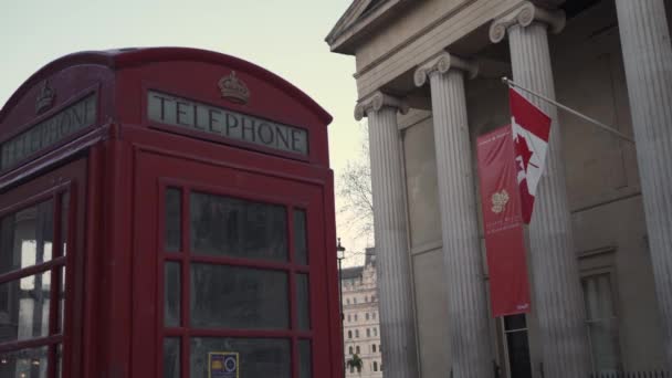 Bandeiras canadenses acenando do Alto Comissariado do Canadá no Reino Unido com a cabine telefônica vermelha em primeiro plano — Vídeo de Stock