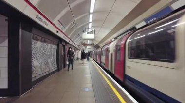 İnsanlar platformda yürürken Oxford Circus istasyonundan ayrılan tren.