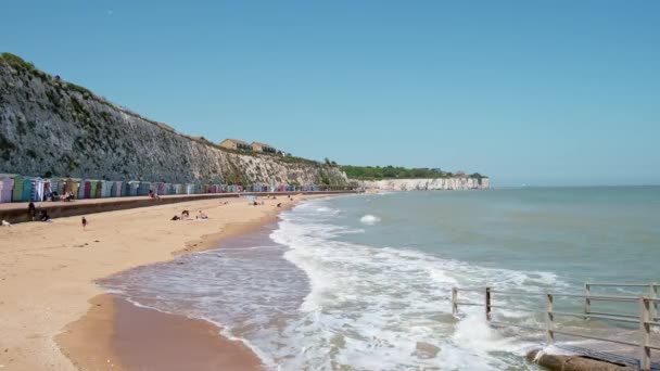 Ludzie cieszą się słonecznym dniem na pięknej piaszczystej plaży we wschodniej Anglii z drewnianymi domkami na plaży — Wideo stockowe