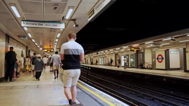 Persone in maschera in attesa di un treno District Line al trafficato binario Victoria Station il giorno d'estate — Video Stock