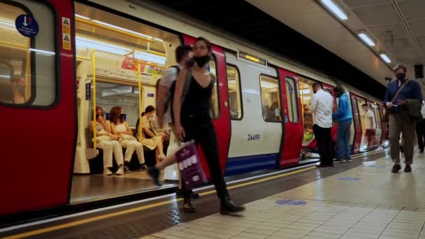 Ludzie w maskach czekają na pociąg District Line na ruchliwej peronie Victoria Station w letni dzień — Wideo stockowe