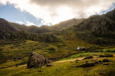 Snowdonia, Galler 2025.09.21 Güneşli uçurumların ve Snowdonia Milli Parkı 'ndaki yuvarlanan tepelerin altındaki engebeli bir vadide tek bir taş kulübe bulunuyor.. 